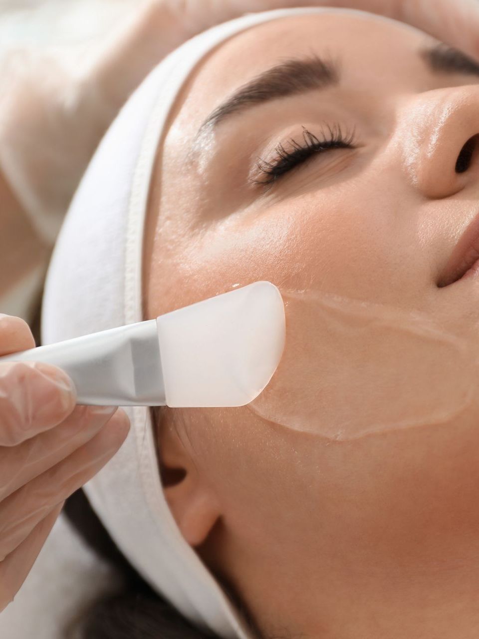 Person receiving a facial treatment; a technician applies a mask to their face with a spatula.