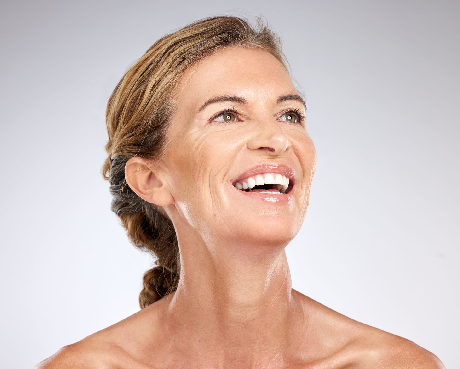 Woman with light skin smiles, looking upward; she has wrinkles.