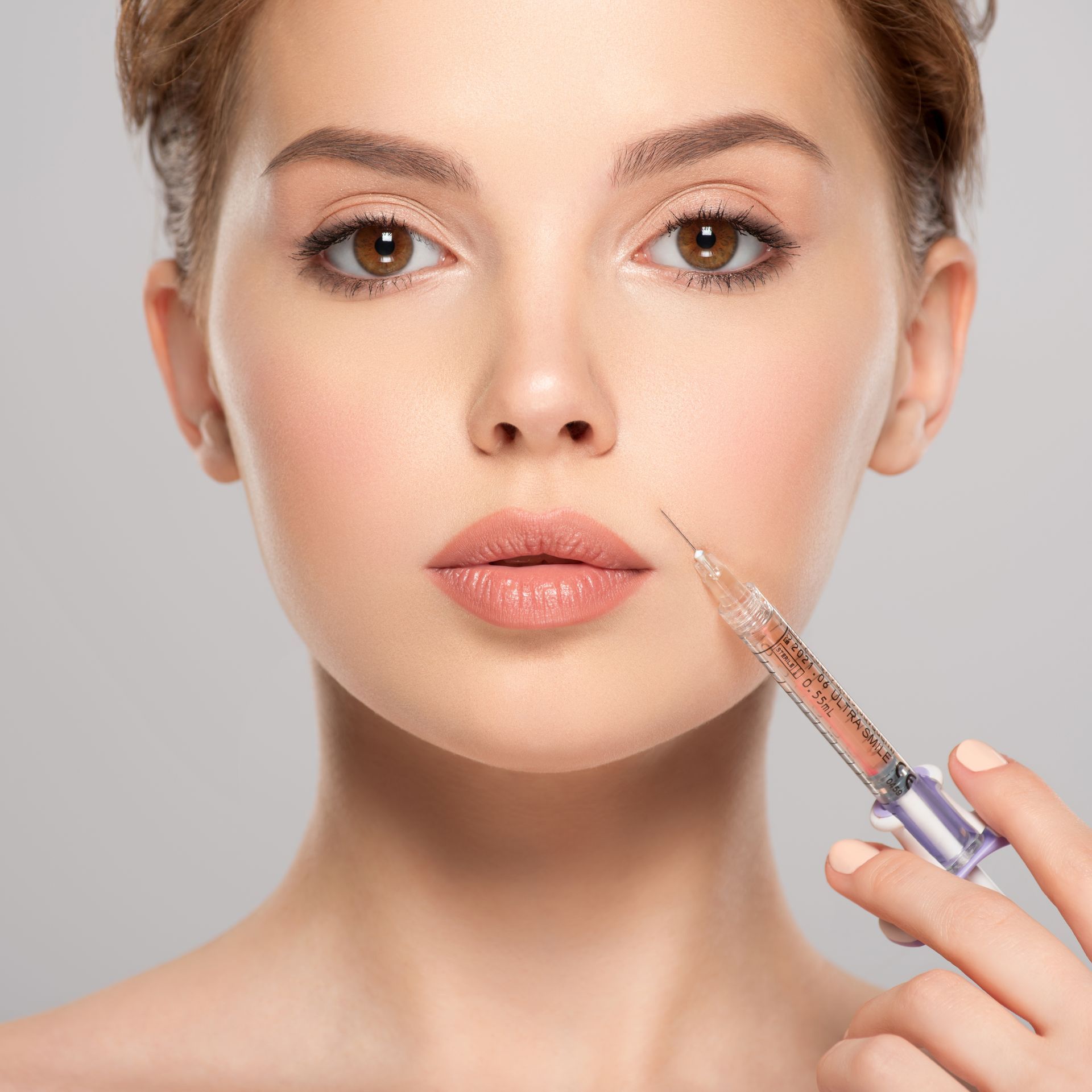 Woman receiving a facial injection in a medical setting, syringe pointed near her lips.