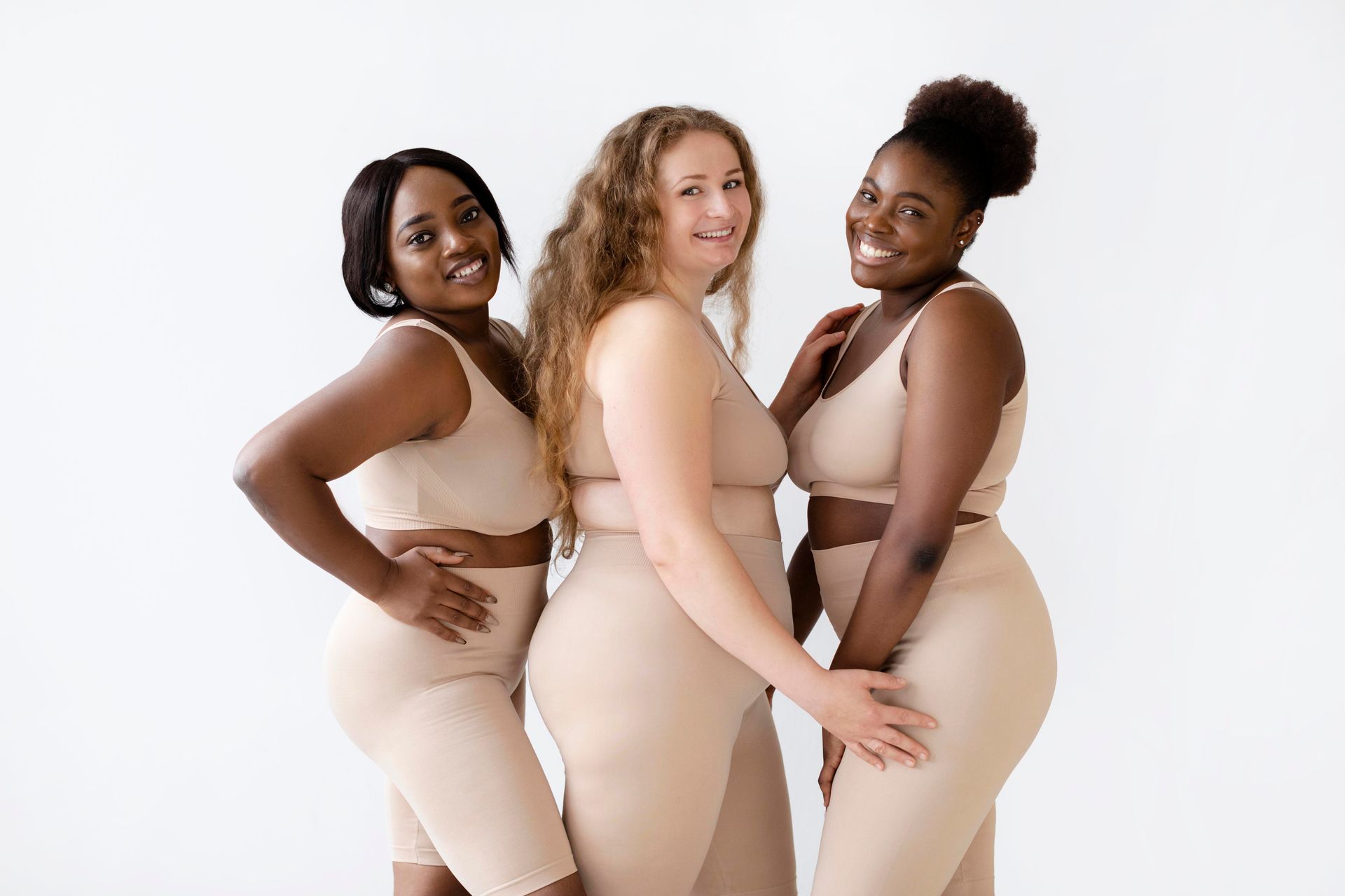 Three women in beige athletic wear smiling, posing together against a white background.
