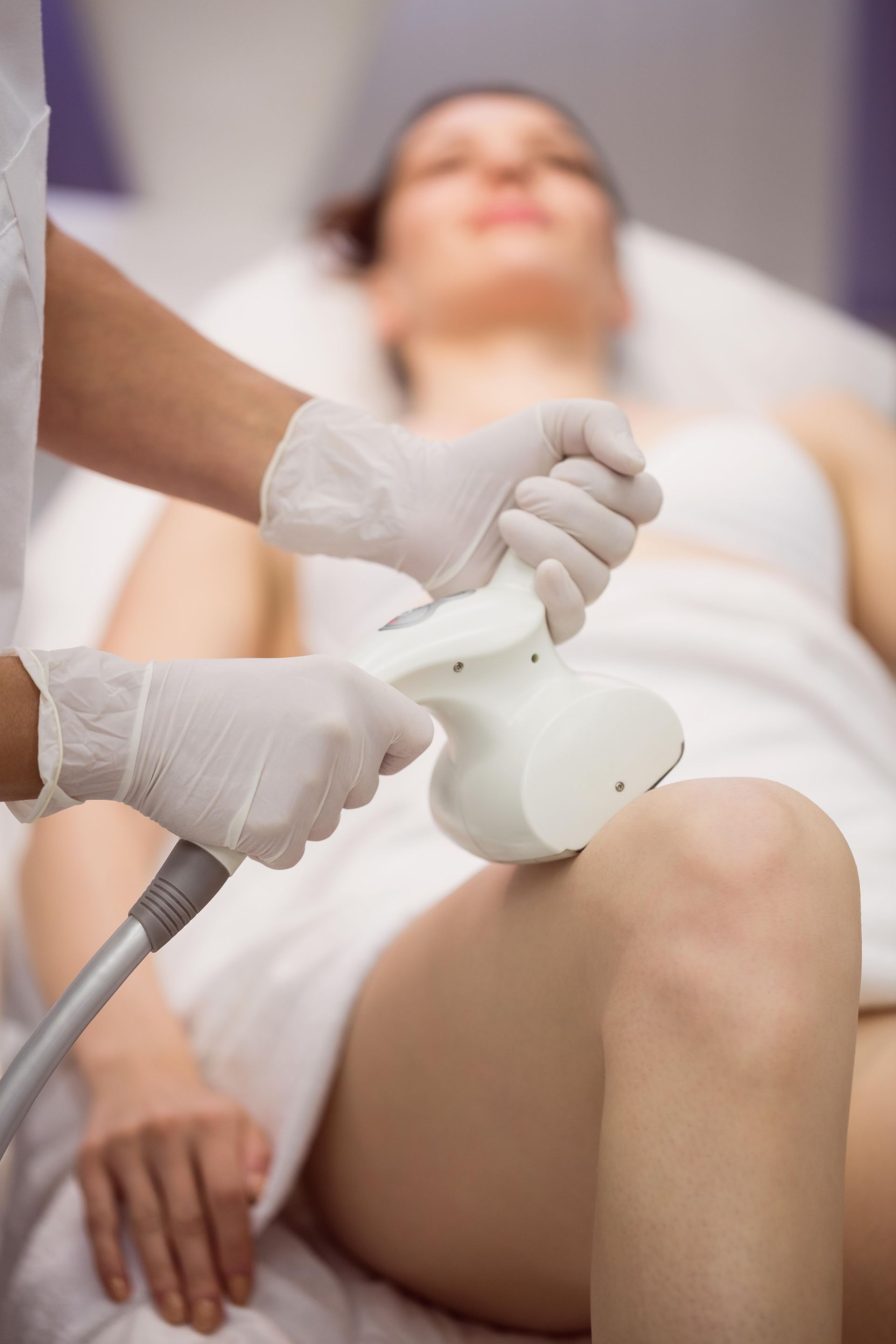 A person receiving cosmetic treatment on their leg with a handheld device, in a clinic setting.