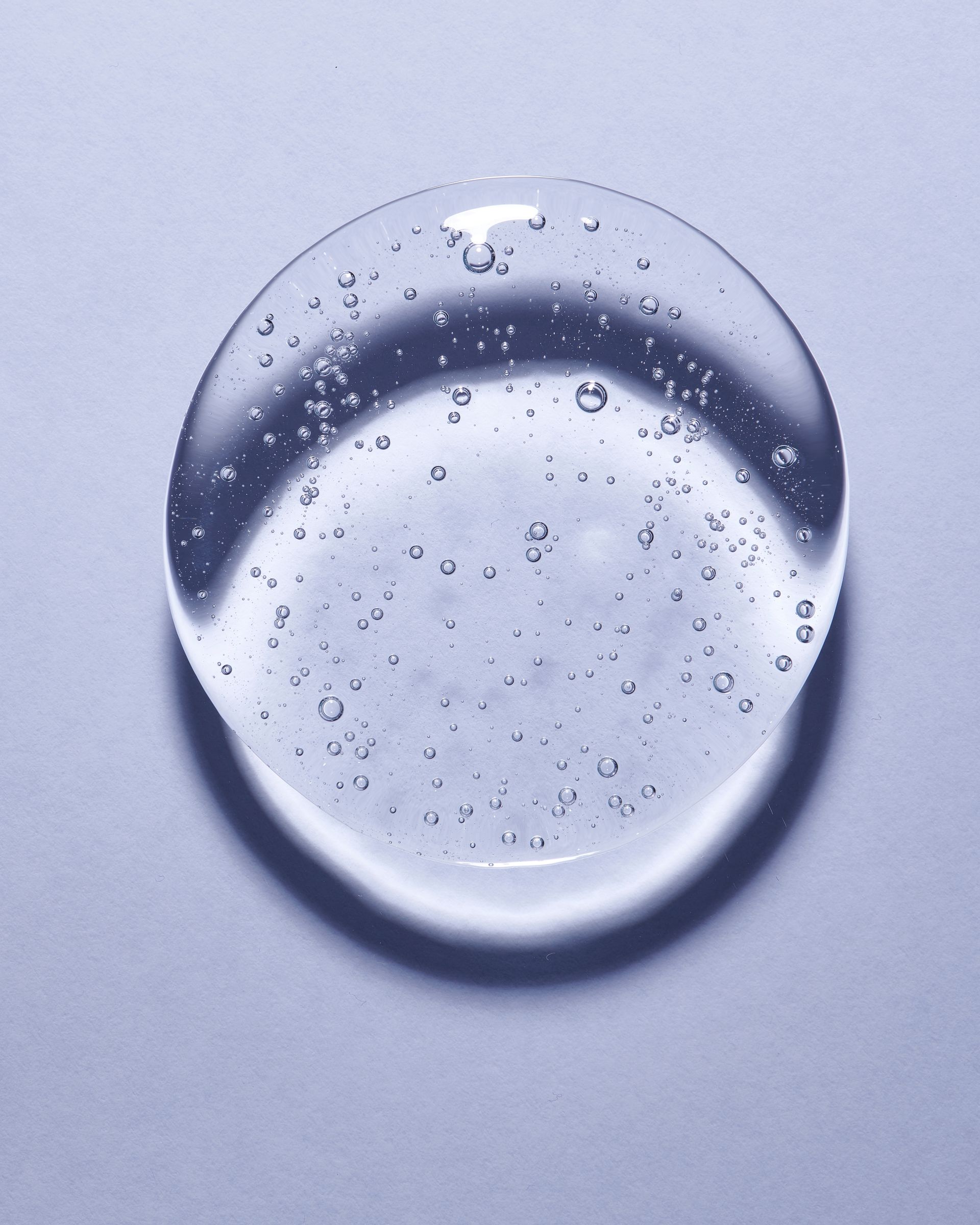 Clear, round gel droplet on a light gray surface, with small air bubbles visible within the gel.