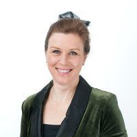 Woman with light brown hair smiles, wearing a green velvet jacket and black top, against a white background.