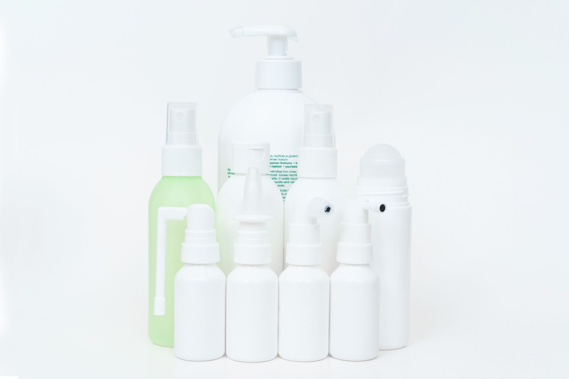 Assortment of white and green cosmetic bottles and spray containers against a white background.