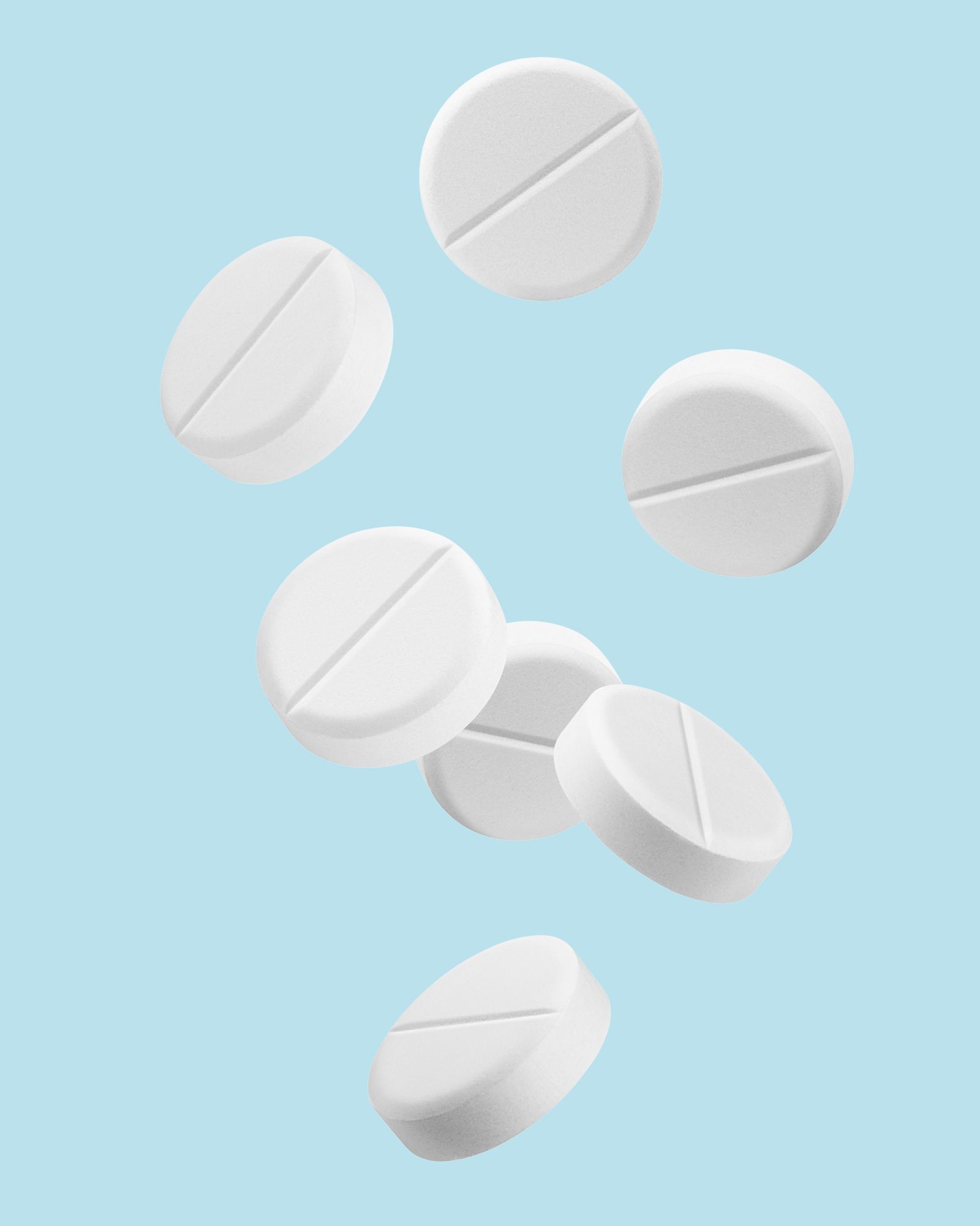 White, circular pills with a scored center floating against a light blue background.