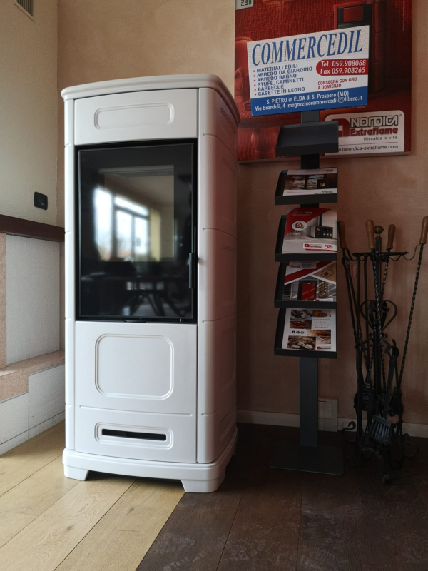 Stufa a legna bianca in un angolo dello showroom con un espositore per brochure e sci in mostra.