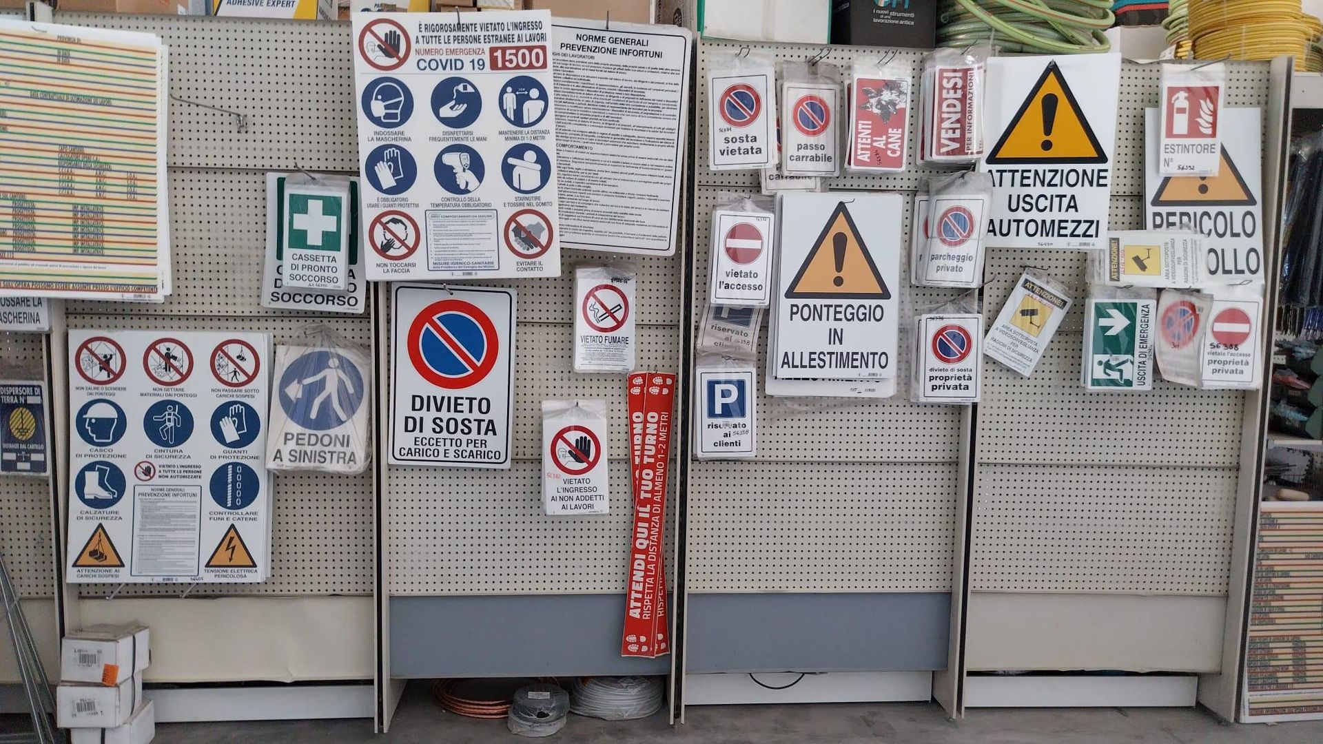 Parete con vari cartelli di sicurezza e di avvertimento esposti su un pannello forato in un negozio o in un magazzino.