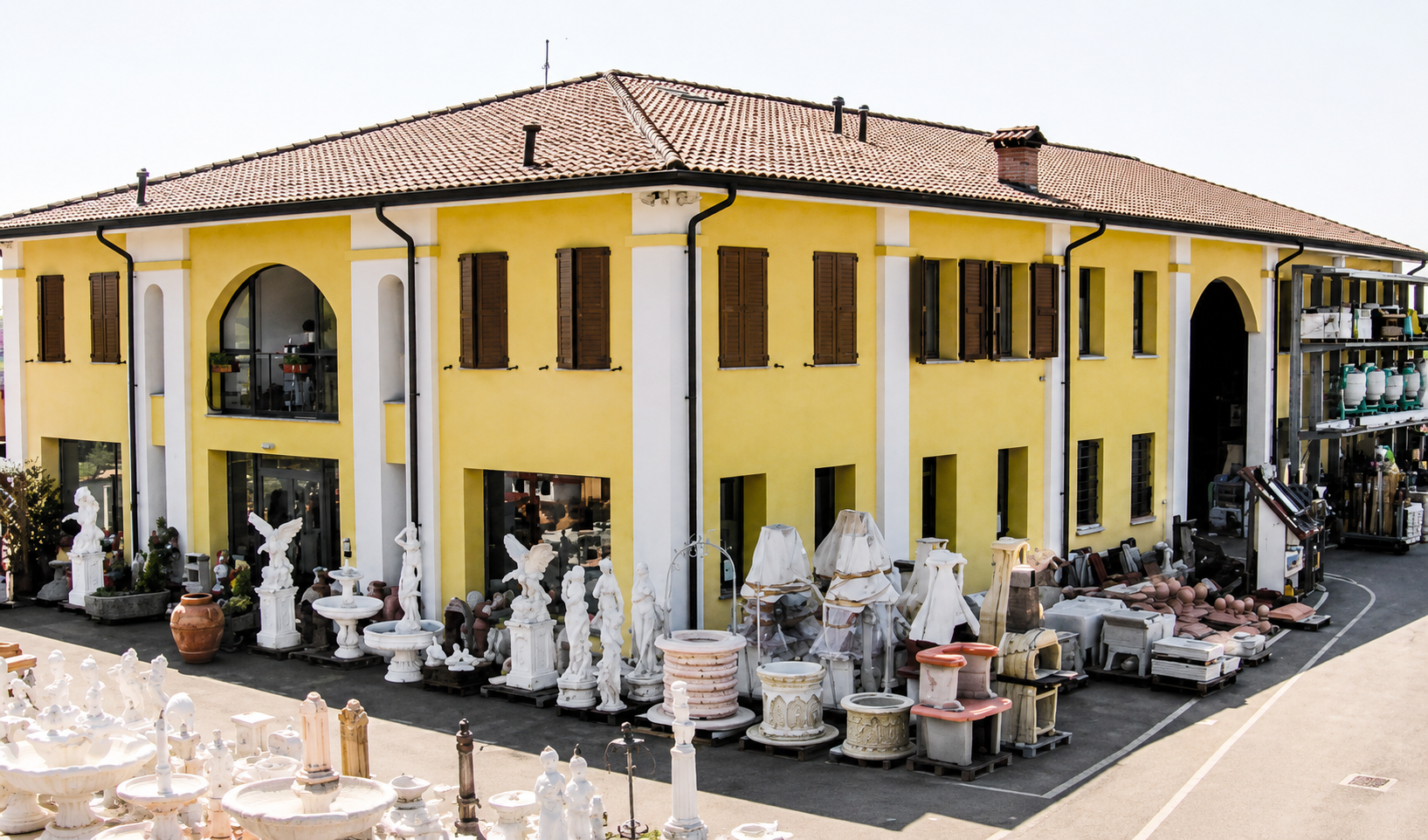 Edificio giallo a due piani con tetto di tegole, circondato da statue da giardino e vetrine di ceramiche.