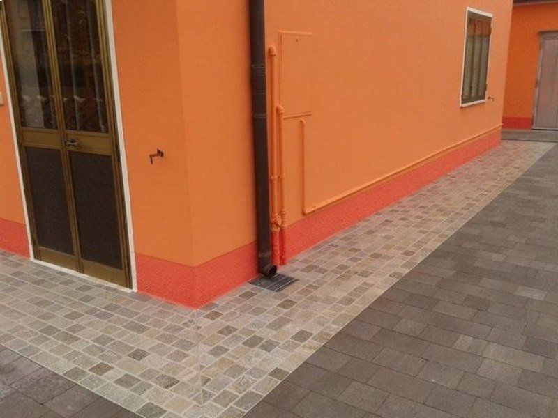 Angolo di edificio arancione con battiscopa rosso, porte e pavimentazione in pietra grigia con motivi decorativi.
