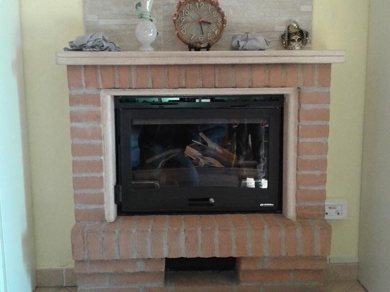 Camino in mattoni con inserto frontale in vetro nero e oggetti decorativi sulla mensola.