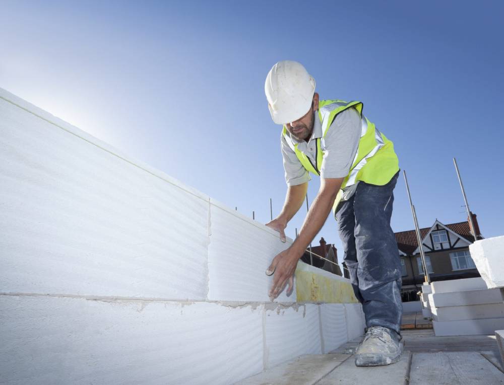 Un operaio con elmetto e giubbotto di sicurezza installa blocchi isolanti bianchi su un tetto.