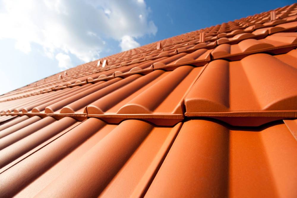 Tegole di terracotta sotto un cielo azzurro, viste dal basso.