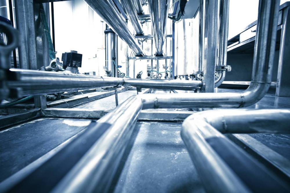 Tubature industriali e travi d'acciaio in un interno di fabbrica metallico con fredde tonalità blu.