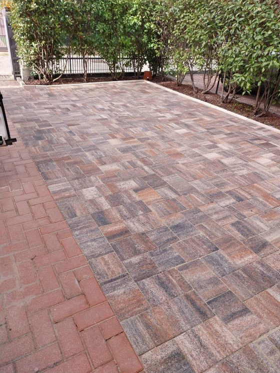 Patio in mattoni e pavimentazione con siepe e recinzione sullo sfondo.