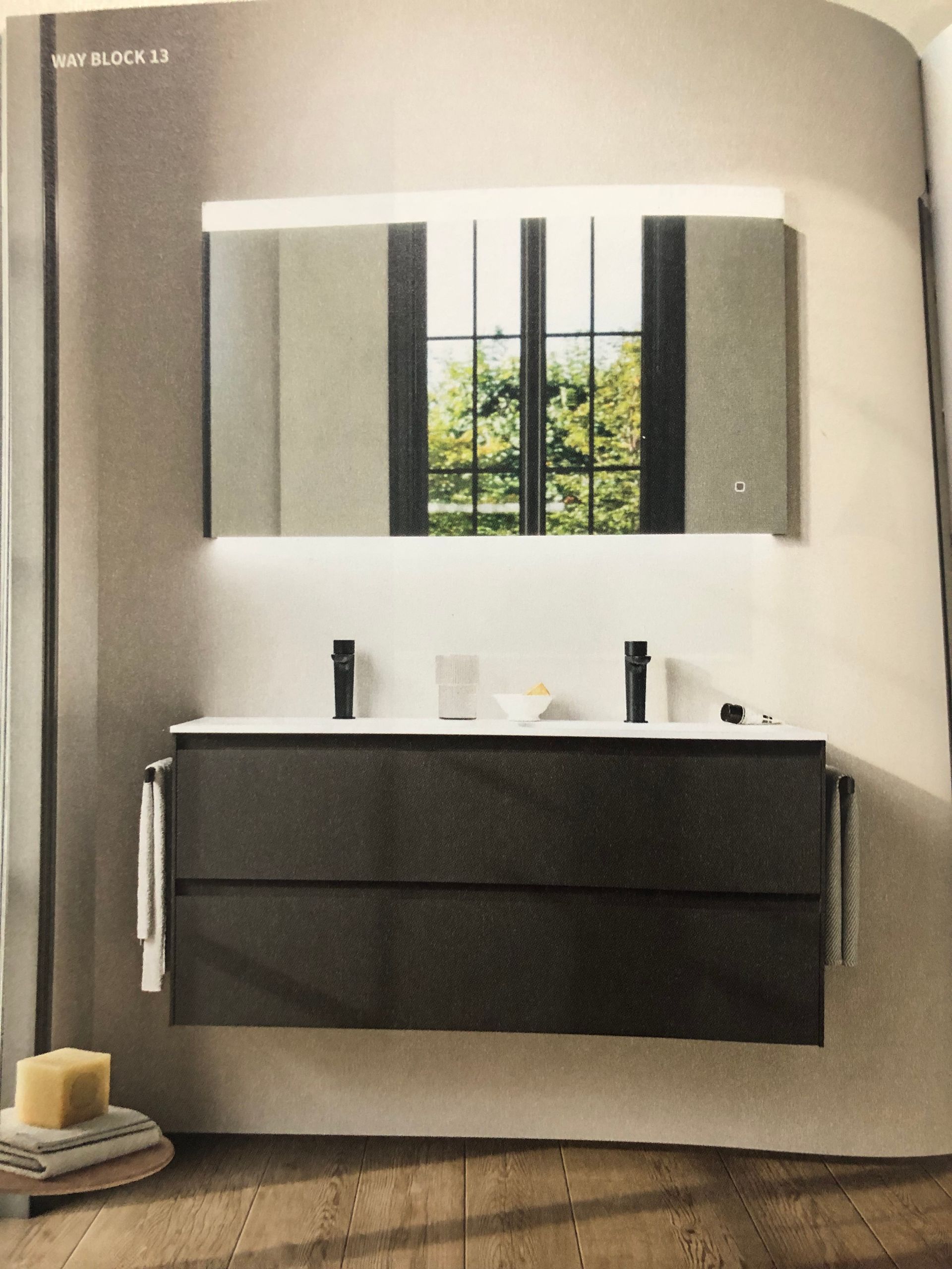 Mobile bagno moderno con ante scure, mobiletto con specchio e finestra riflessa nello specchio.