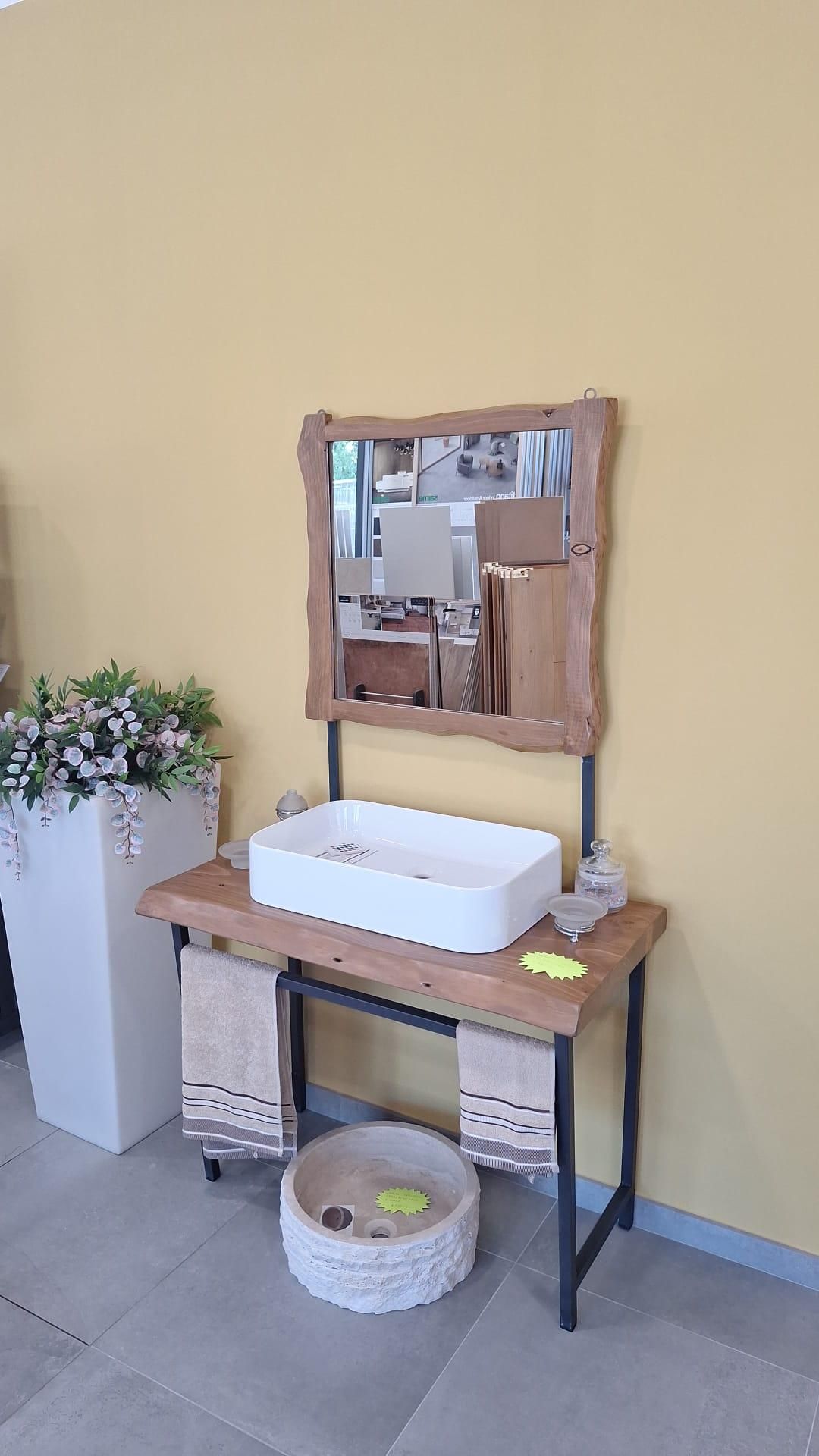 Piccola postazione lavabo con tavolo in legno, lavabo bianco, specchio, piante in vaso e un cesto intrecciato sottostante.