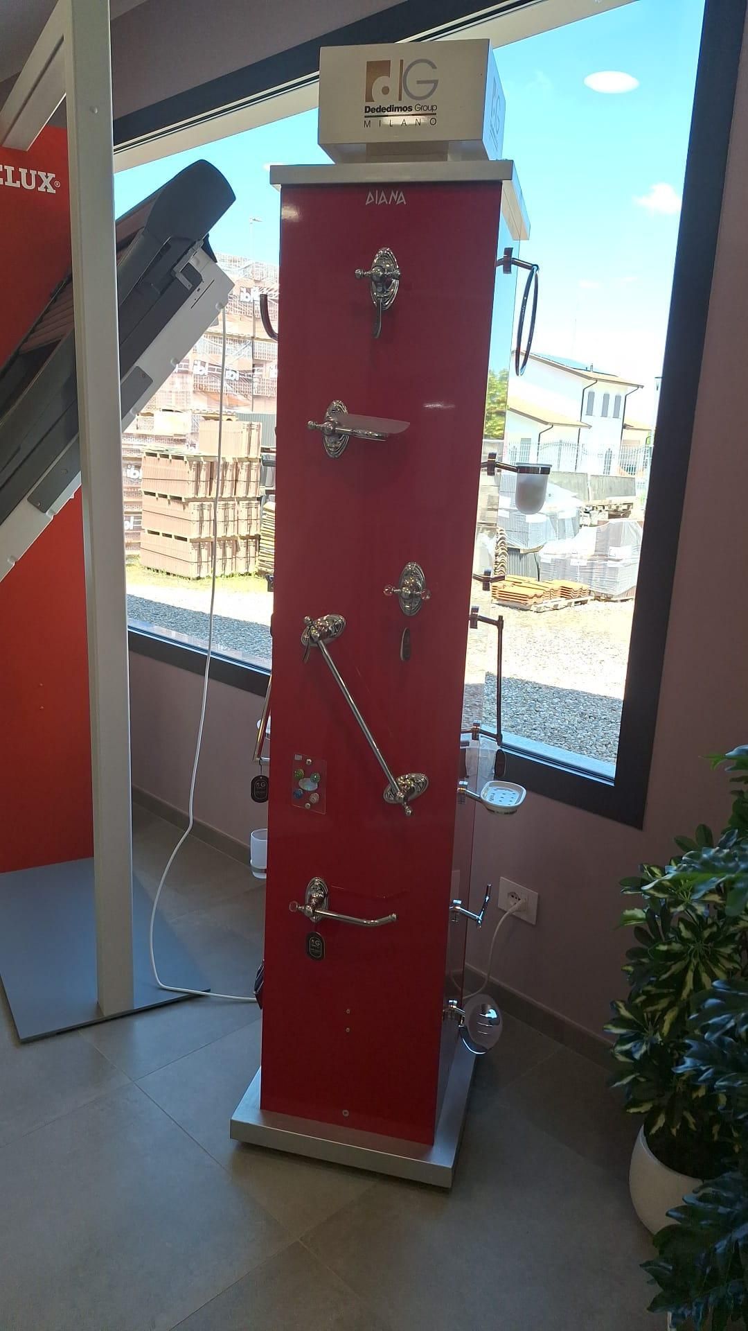 Alto espositore rosso con accessori metallici montati, posizionato vicino a una grande vetrina in uno showroom.
