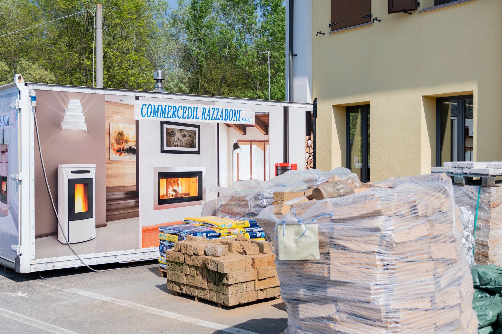 Materiali da costruzione accatastati accanto a un edificio prefabbricato bianco con decorazioni murali in un parcheggio.