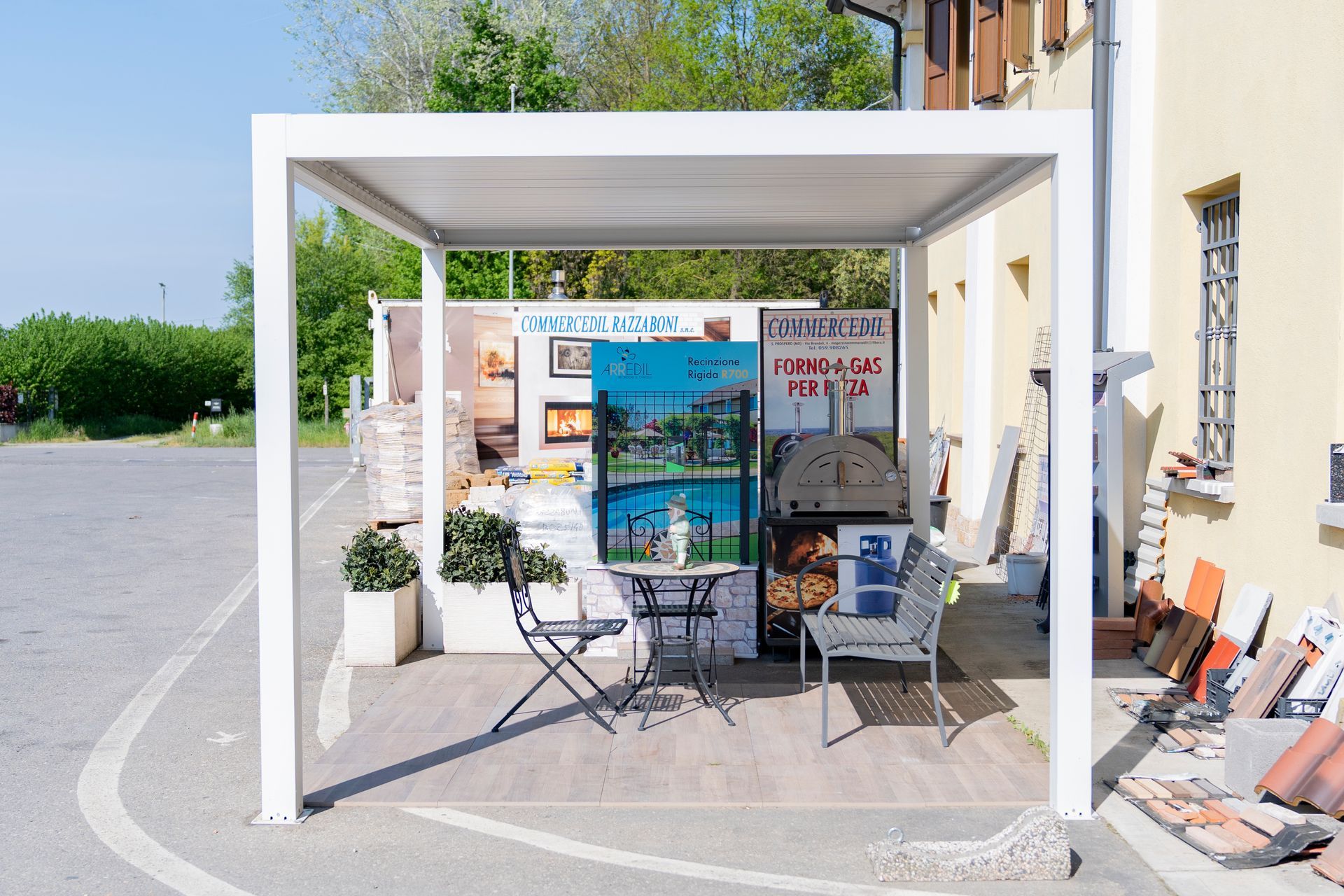 Chiosco all'aperto con brochure e sedie pieghevoli sotto una tettoia bianca su un marciapiede soleggiato