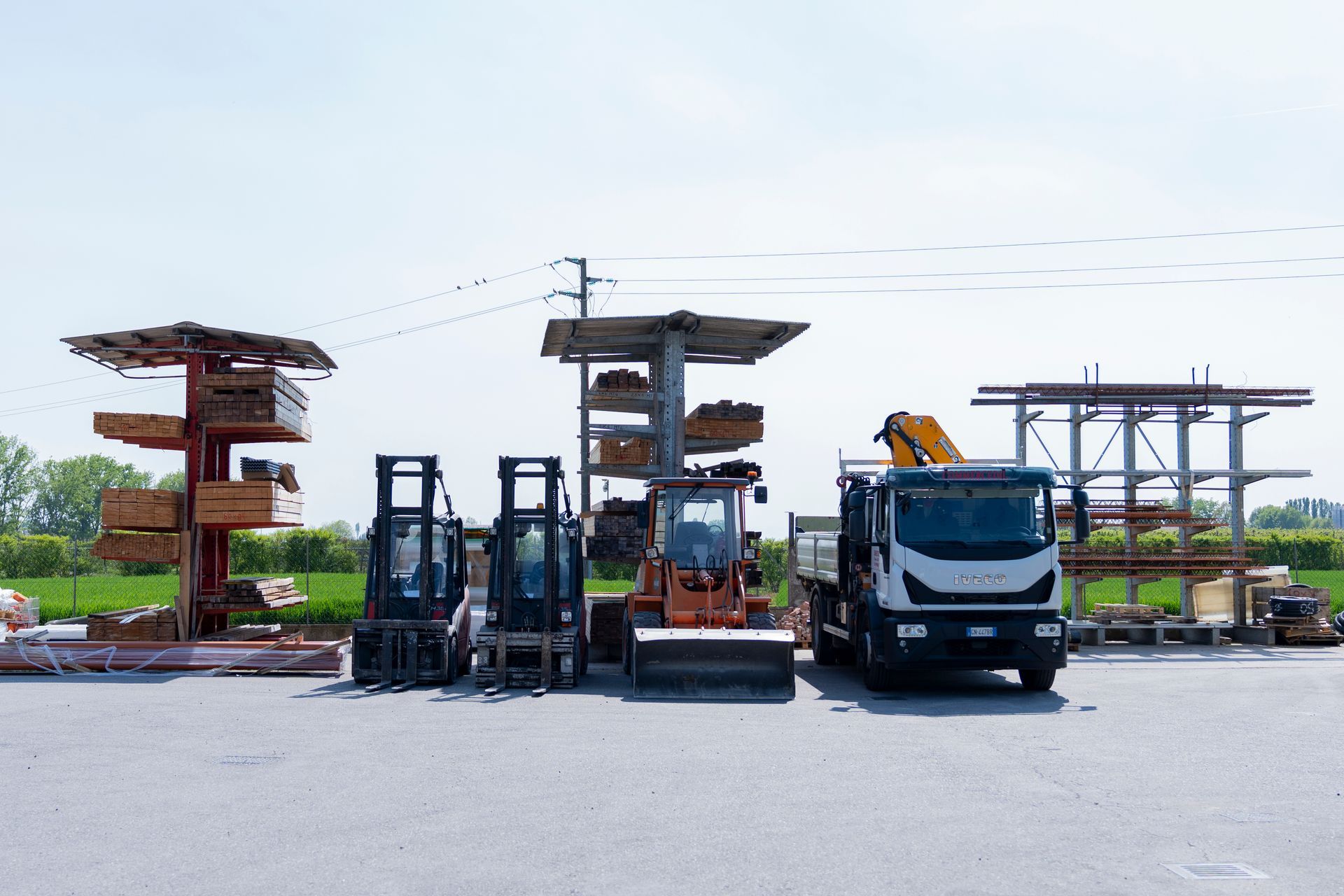 Un carrello elevatore è parcheggiato accanto a strutture di legno impilate e a un camion in un parcheggio all'aperto.