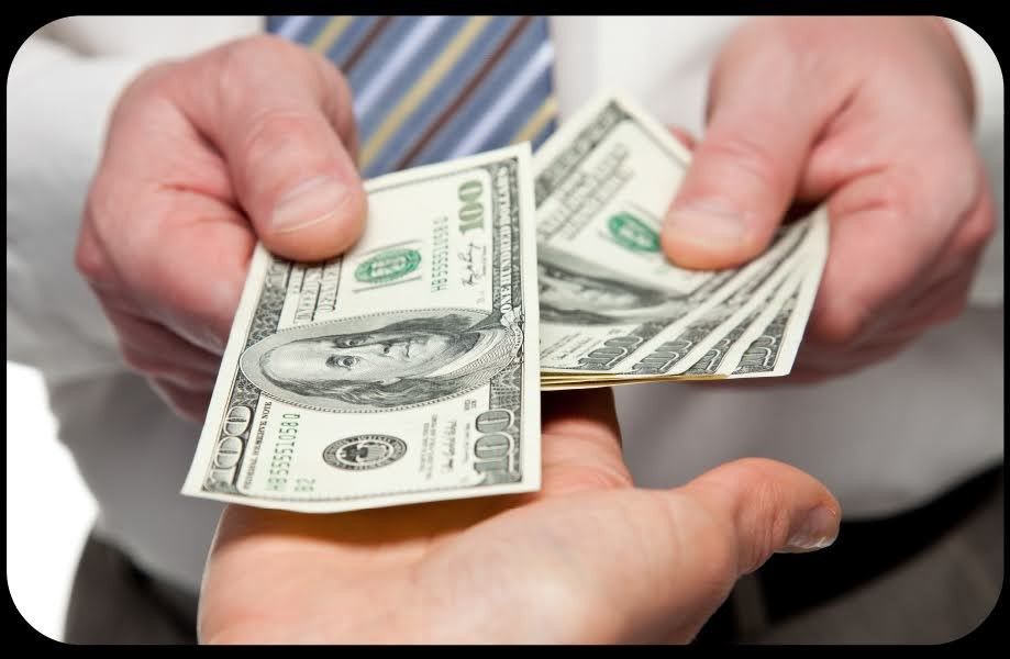 Hands holding out and receiving several $100 bills. A person in a striped shirt is giving cash to another.