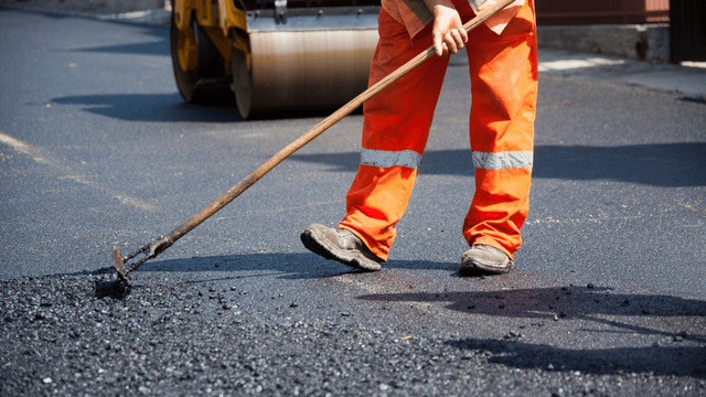 Construction worker in orange safety gear raking freshly laid asphalt to create an even surface during an asphalt paving service in Arvada, CO