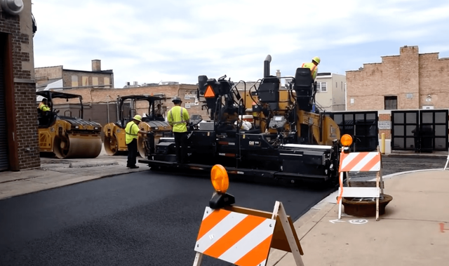 Large paving machine laying fresh asphalt on a city street while workers monitor the process during an asphalt paving service in Arvada, CO