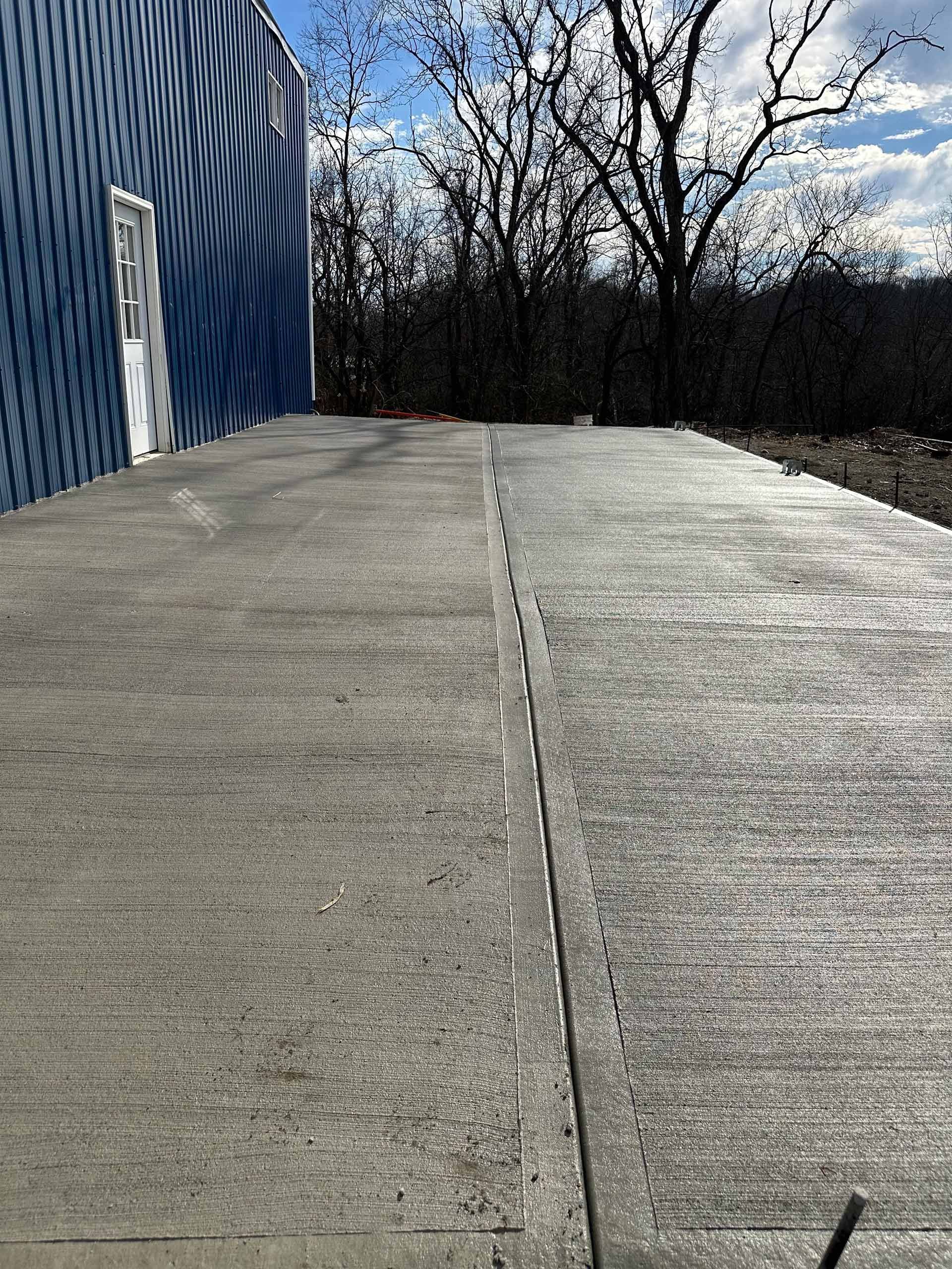 A concrete walkway leading to a blue building with trees in the background.