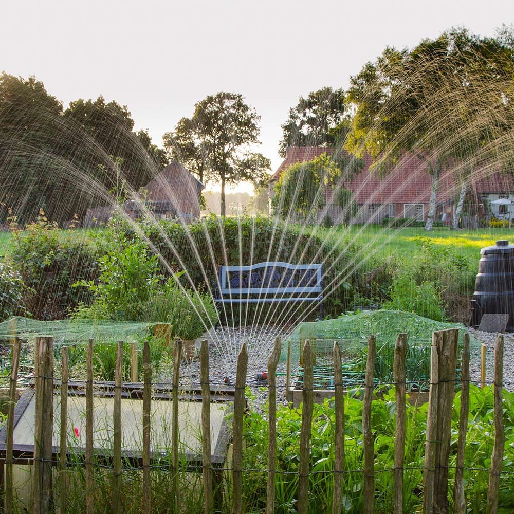 Professional Irrigation Service In Cincinnati, Oh A sprinkler is spraying water in a garden next to a wooden fence.