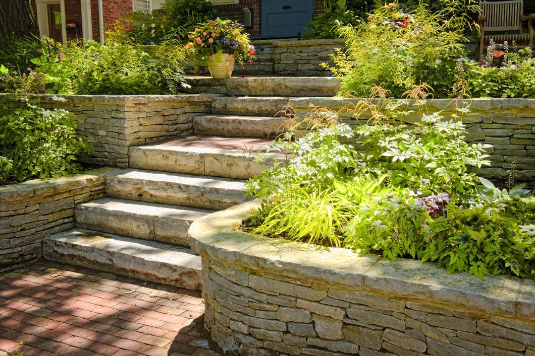 A stone wall surrounds a set of stairs leading up to a house.