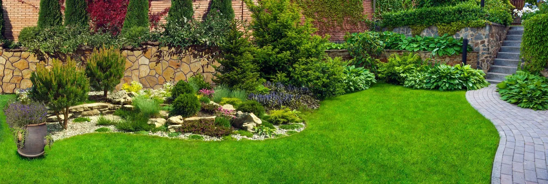 A lush green garden with a brick walkway leading to a house.