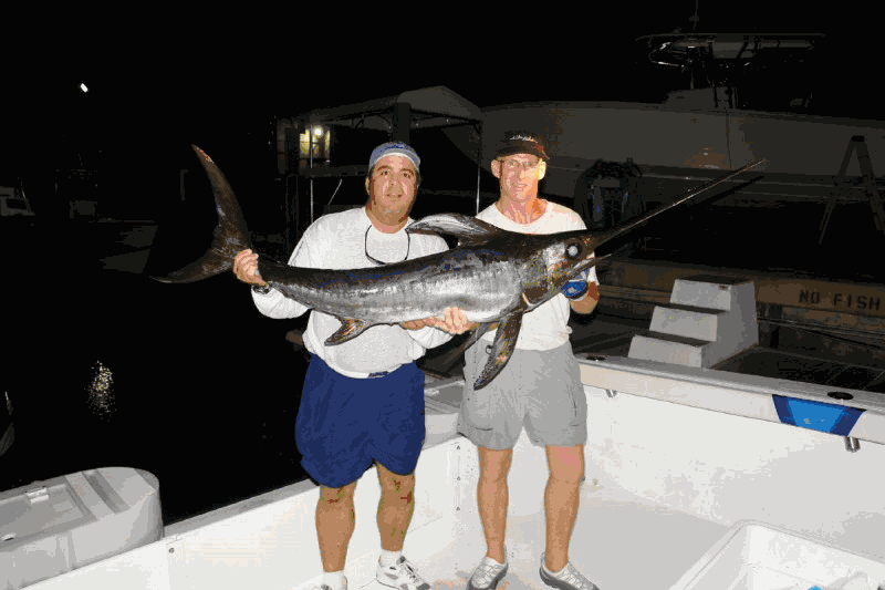 Two men standing on a boat holding a large fish