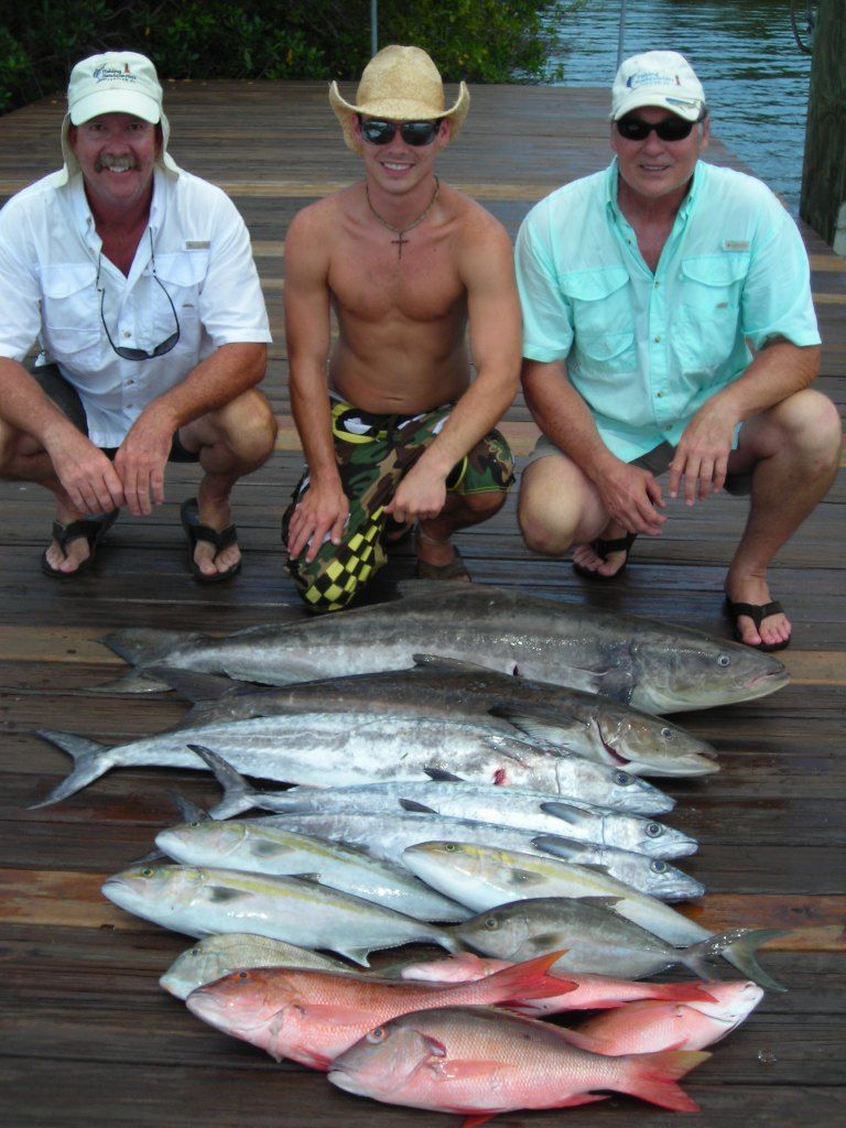 Three men squatting down next to a pile of fish