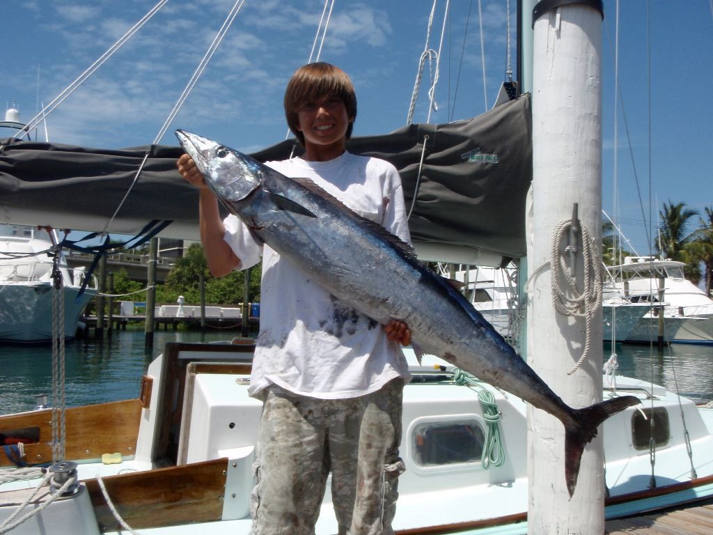 A boy holding a large fish in front of a boat