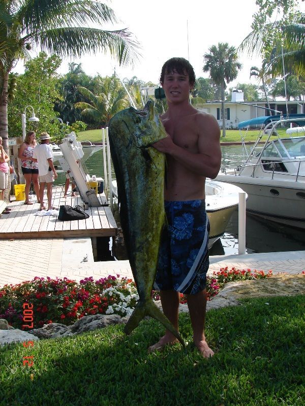 A shirtless man holding a large fish in front of a boat