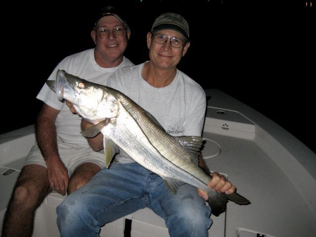 two men sitting on a boat holding a large fish