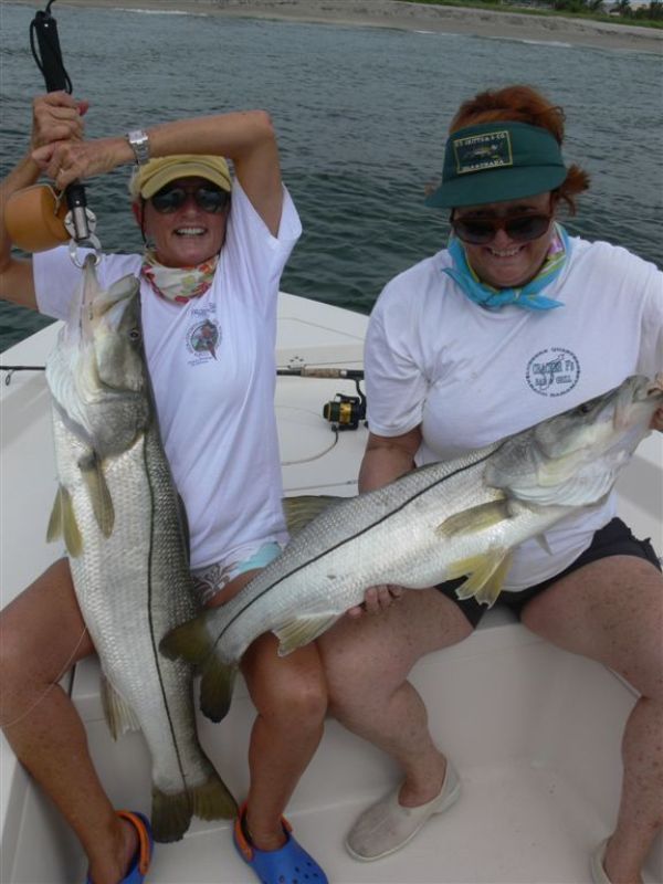 two women sitting on a boat holding large fish