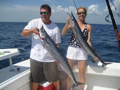 A man and a woman holding two large fish on a boat