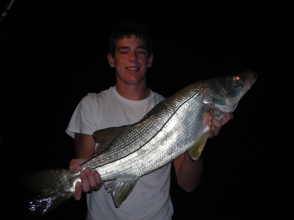 A young man in a white shirt is holding a large fish