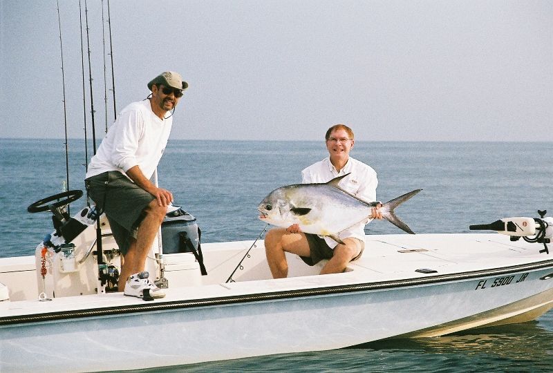 Two men sitting on a boat holding a large fish