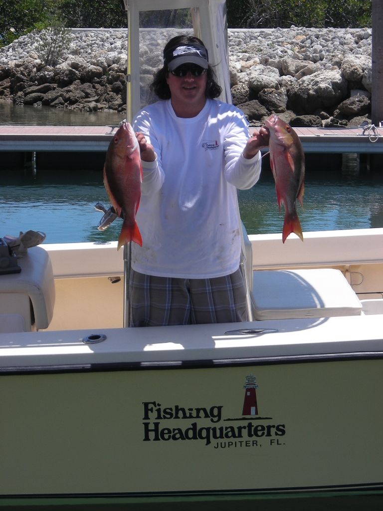 A man holding two fish in front of a boat that says fishing headquarters