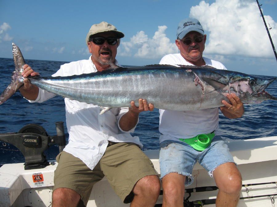 Two men sitting on a boat holding a large fish