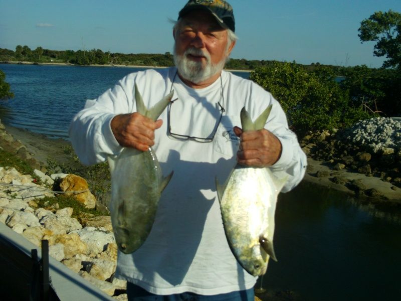 A man is holding two fish in his hands in front of a body of water