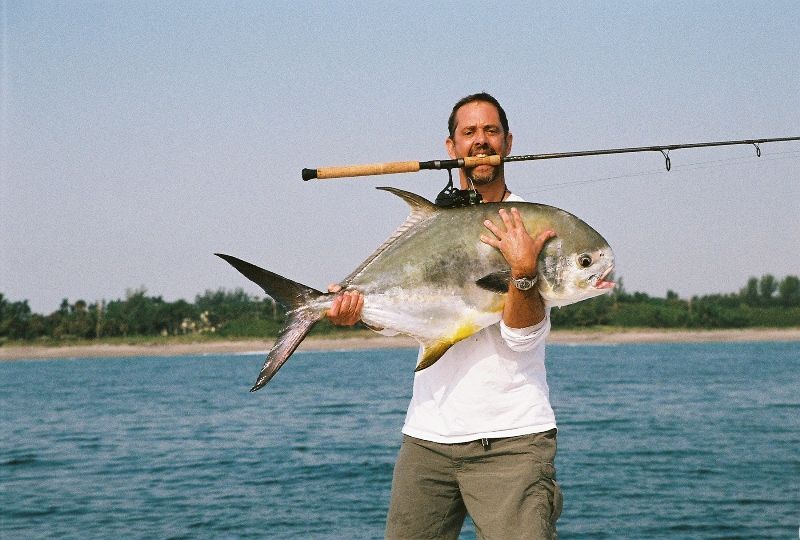 A man holding a large fish with a fishing rod in his mouth