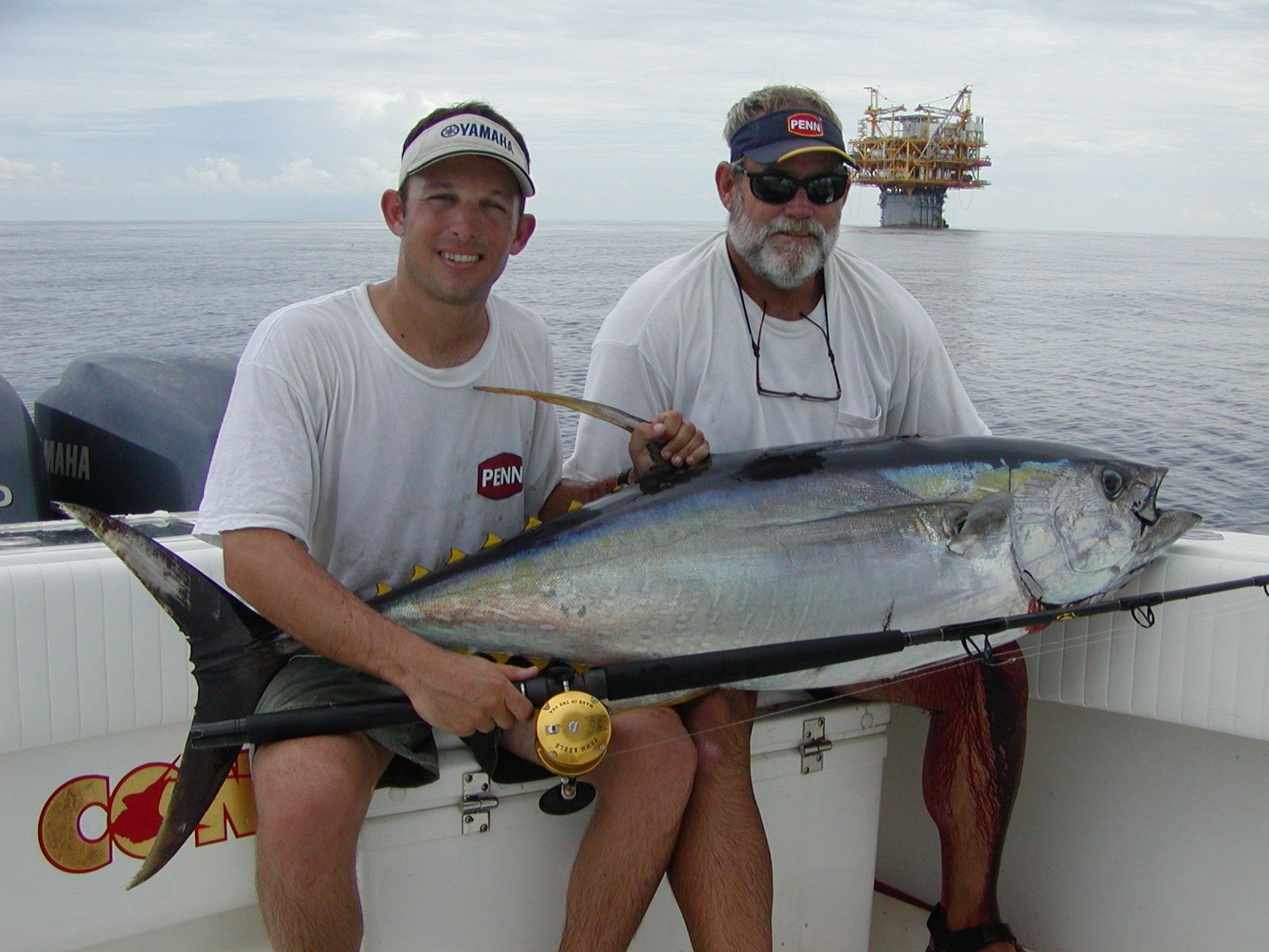 Two men sitting on a boat holding a large fish