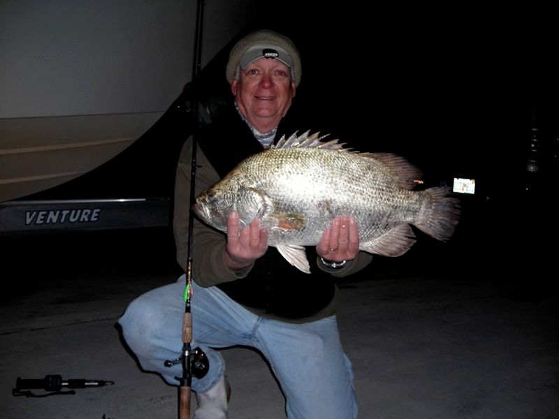 A man holding a large fish in front of a boat that says venture