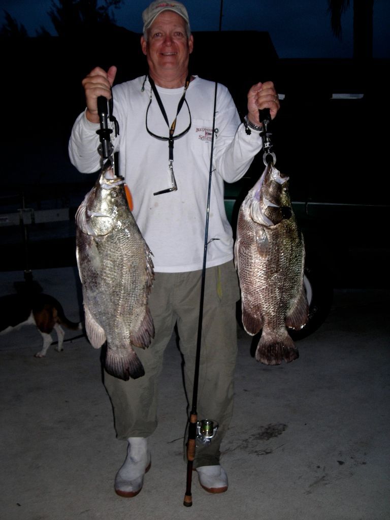 A man in a white shirt is holding two large fish