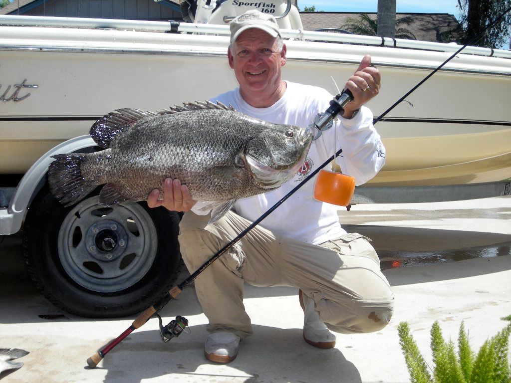A man holding a large fish in front of a boat that says scout
