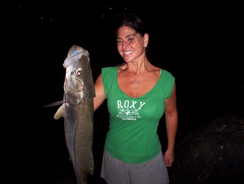 A woman in a green roxy shirt is holding a large fish