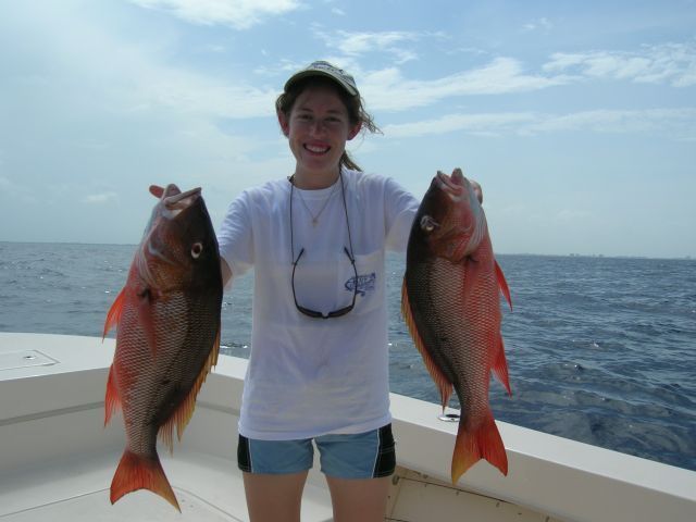 A woman on a boat holds two fish in her hands